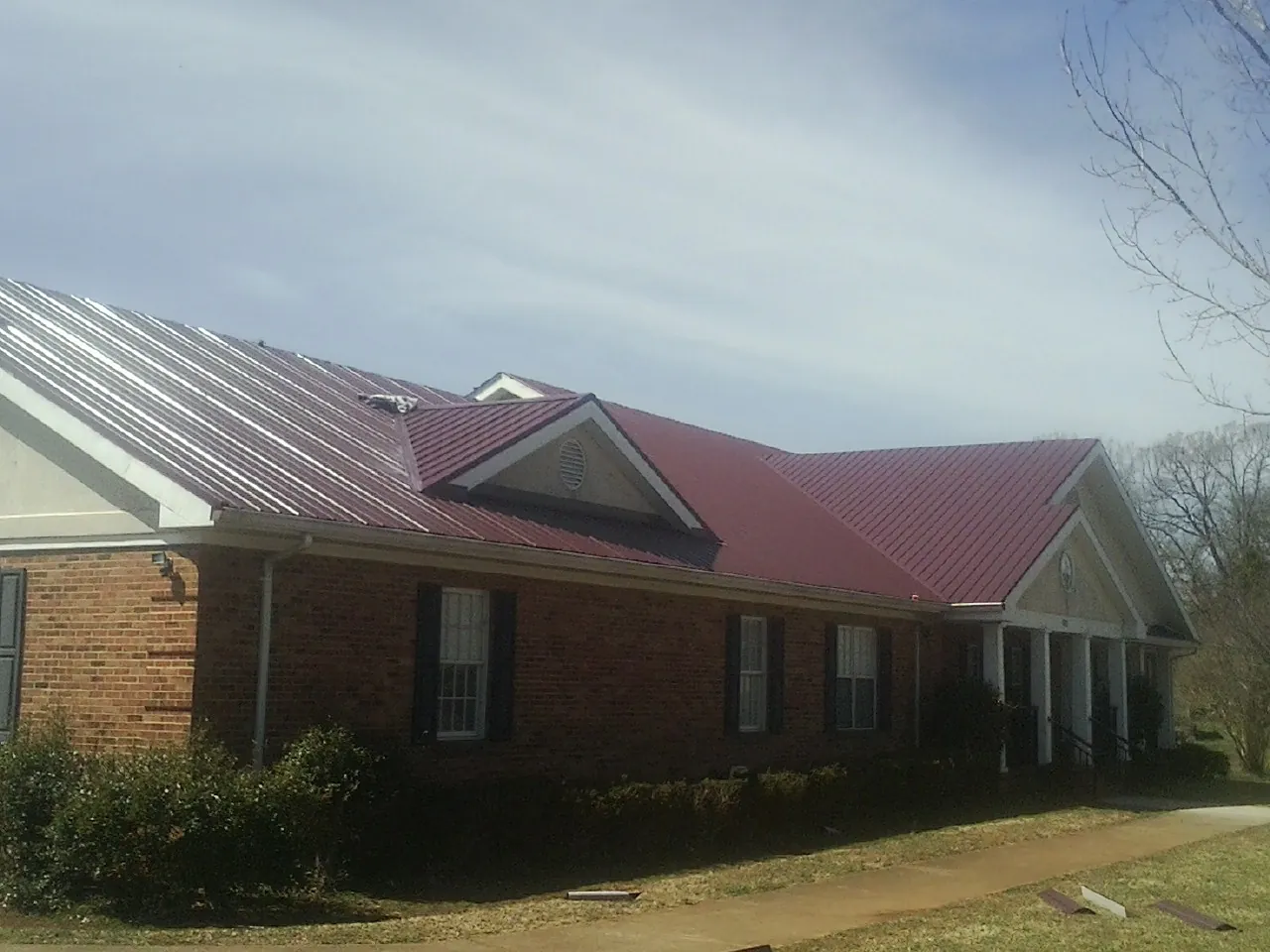Red metal roof with gabled entries on a long brick building, from a Hail Damage Roof Repair job in Santa Ysabel