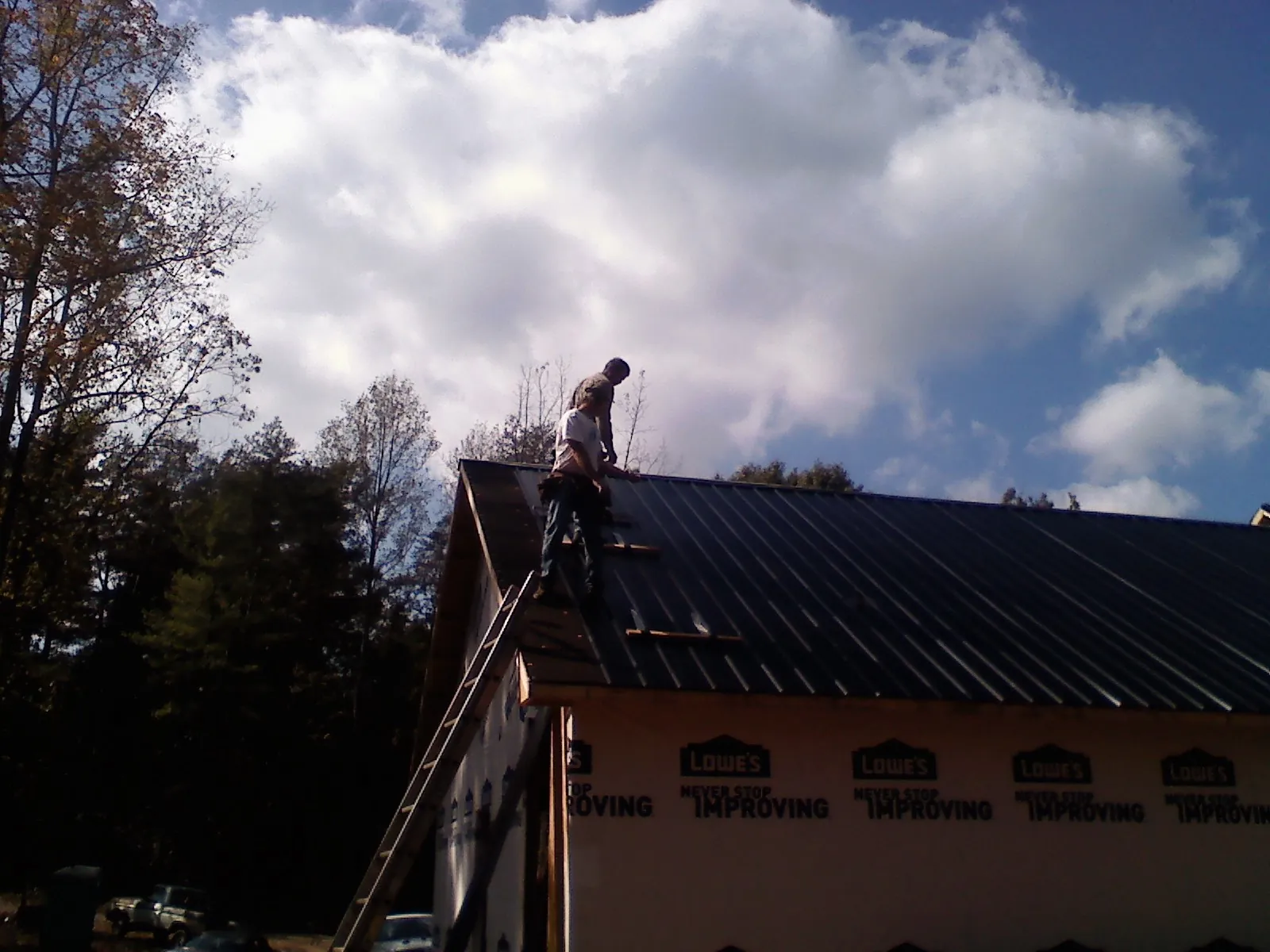 Roofer fastening dark metal panels high against a cloudy sky, from a Roof Inspection job in Santa Ysabel