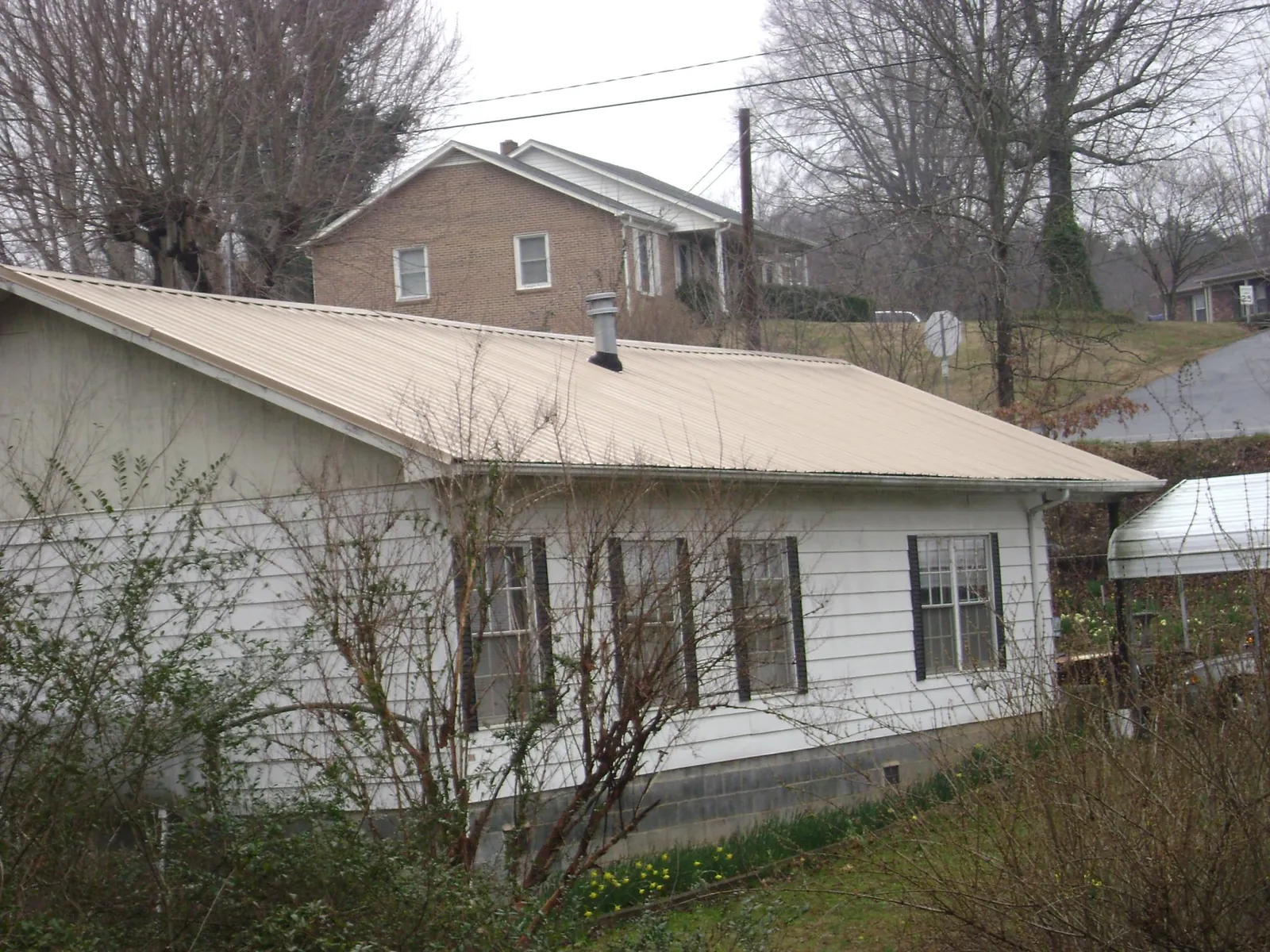 Tan metal roof on a white sided house set into a hillside — Commercial Roofing by Roofing Brothers in Santa Ysabel